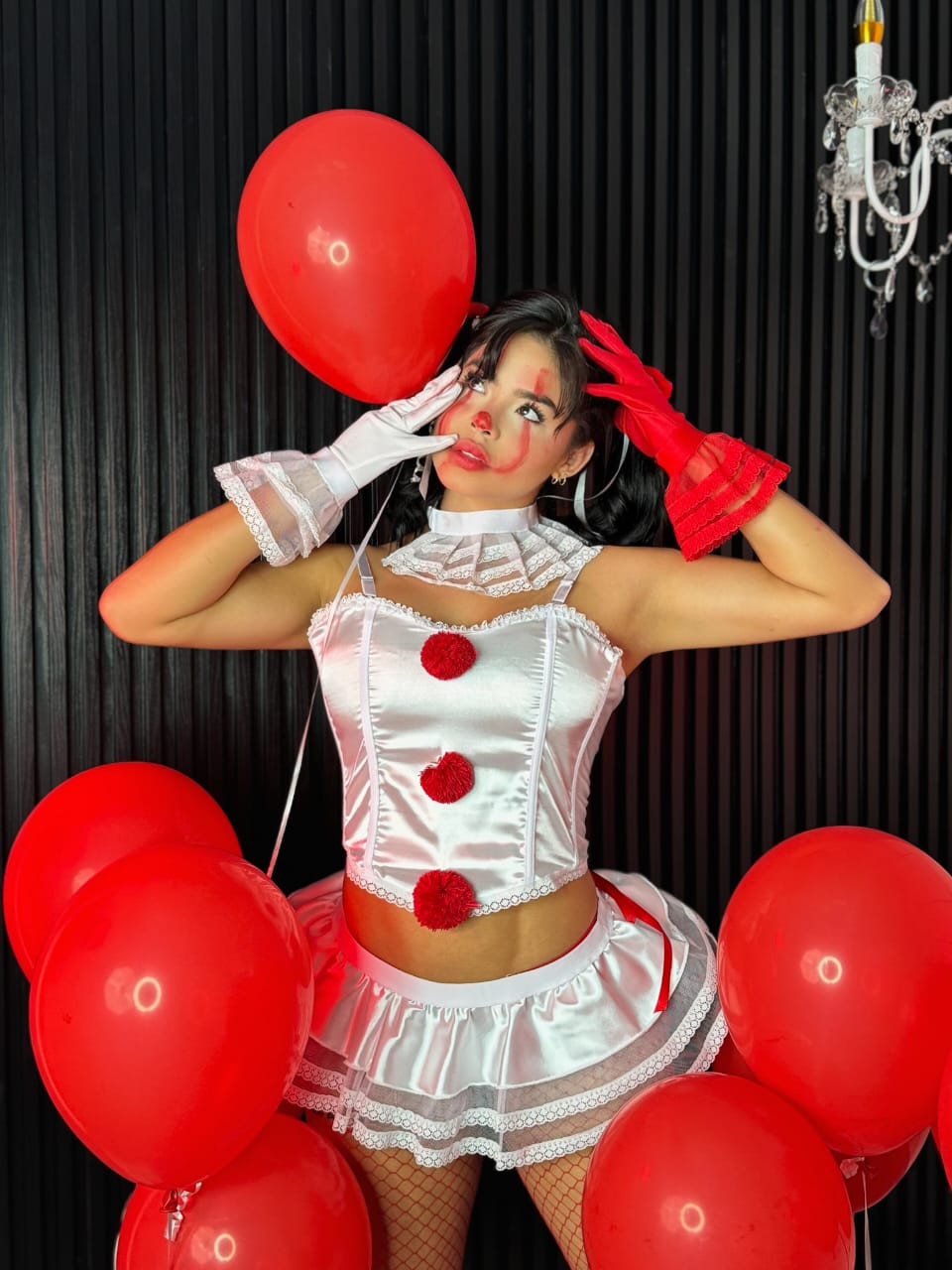 Disfraz blanco y rojo inspirado en IT con top de pompones, minifalda, cuello con volantes y guantes; ambientación con globos rojos.