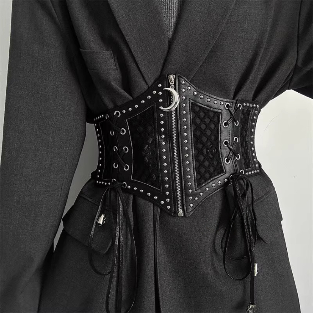 Corset negro de malla con tachas, cordones laterales y detalle de luna sobre vestido negro.
