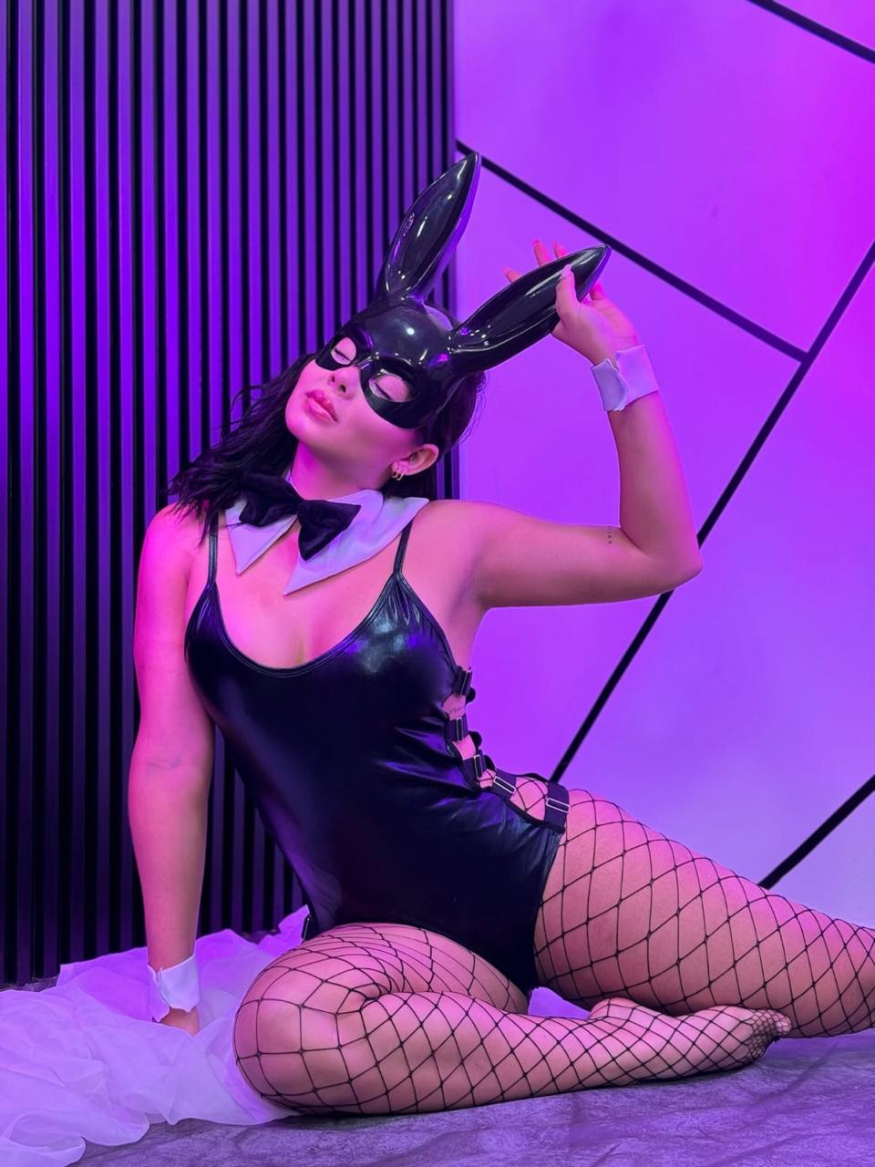 Disfraz de conejita negra con body brillante, hebillas laterales, antifaz de orejas largas, cuello con corbatín y puños blancos.